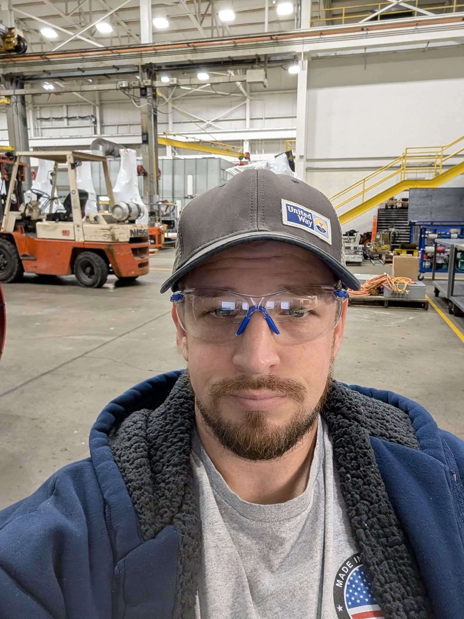 Andrew Fitzgerald on the factory floor wearing safety glasses and a United Way cap